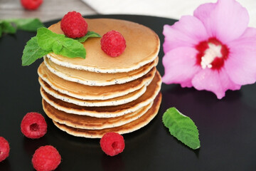 Pancakes with fresh raspberries, mint and jam on a black table with lonicera