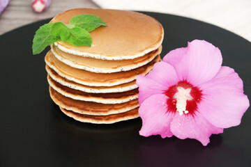Pancakes with fresh raspberries, mint and jam on a black table with lonicera