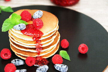 Pancakes with fresh raspberries, mint and jam on a black table with lonicera