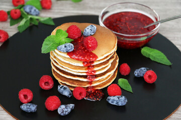Pancakes with fresh raspberries, mint and jam on a black table with lonicera