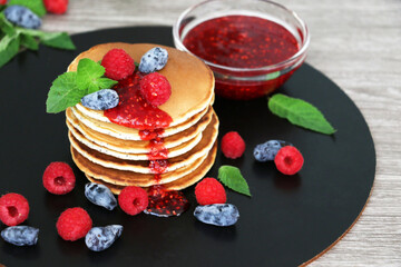Pancakes with fresh raspberries, mint and jam on a black table with lonicera