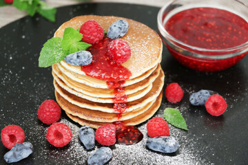 Pancakes with fresh raspberries, mint and jam on a black table with lonicera