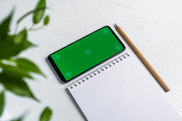 Green leave with blank notepad smartphone green screen mockup and pencil flat lay. Top view