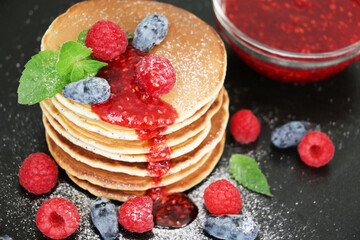 Pancakes with fresh raspberries, mint and jam on a black table with lonicera