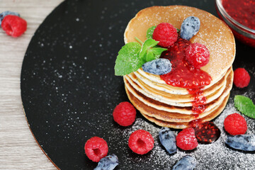 Pancakes with fresh raspberries, mint and jam on a black table with lonicera