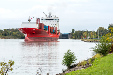 Large container ship sailing up a navigable canal on a cloudy autumn day. A lock is visible in background. Welland Canal, ON, Canada.