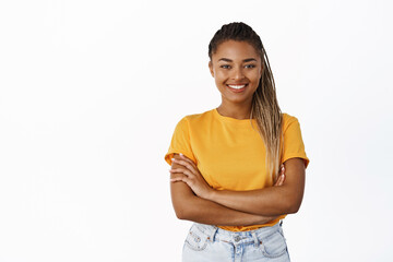 Smiling Black girl in yellow t-shirt standing confident, looking happy and confident, arms crossed over chest, white background - 481002383