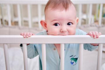 Baby gnaws at the edge crib during teething itching. Funny child scratching his teeth on the rail...