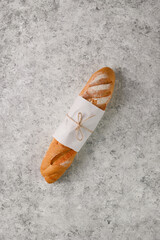 one fresh baguette in paper on textured gray textured