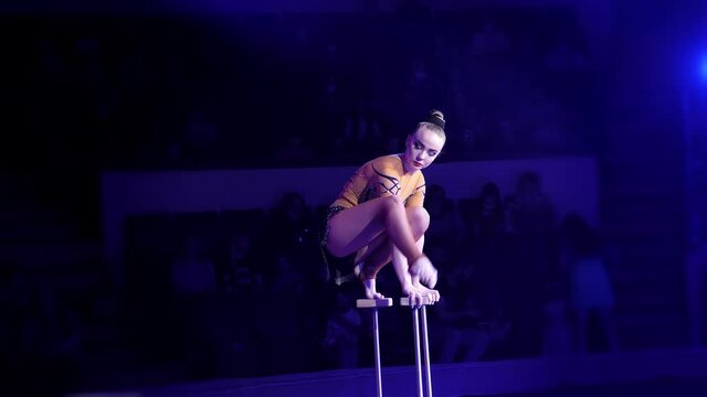 Performance of a female acrobat in a circus. A beautiful acrobat in a bright costume performs in the circus arena with acrobatic numbers, creates a show for the audience. An energetic show. cube