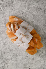 Three fresh baguettes in paper on a gray textured background in the center of the frame. They lie...