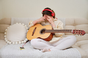 A shamed crying woman with acoustic guitar sitting on a bed in a home living room