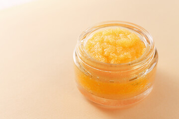 Homemade orange sugar scrub in a glass container on a plain background with copy space. Cosmetic product for peeling and spa treatments.