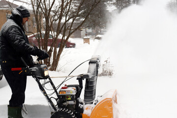 senior man snow blowing driveway during storm.