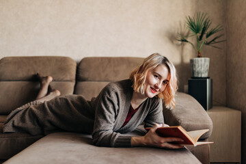 Obraz premium Thoughtful student girl reading book. Young woman studying at home, sitting on beige couch