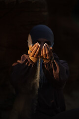 A woman in a hijab pours sand from her hands on a dark background. Front view 