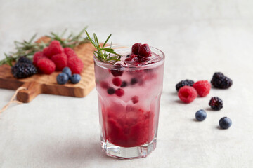 A glass of Red Fruits Soda Blackberry cocktail with berries and strawberry, lime and mint on grey background.