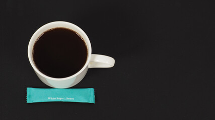 Hot coffee in white cup and white sugar sachet on black blackground.