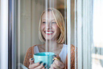 beautiful woman drinking coffee in the morning sitting by the window. view from outside.