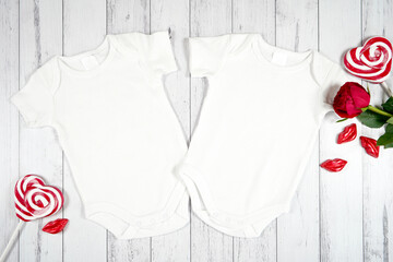 Baby two twins romper onesie jumpsuit product mockup. Valentine's Day farmhouse theme SVG craft product mockup styled with red rose and heart shaped lollipops against a white wood background. Flatlay.