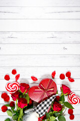 Valentine's Day farmhouse theme background styled with red roses, heart shaped gift, and buffalo plaid gnome against a white wood background. Creative composition flat lay vertical backgroud.