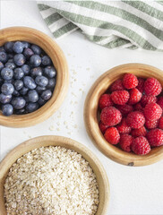 wooden bowl with fruits and cereals on a white background, blueberries, raspberries and oatmeal, healthy breakfast