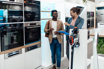 African American man talking with salesman about built-in oven he wants to buy in electronics and...