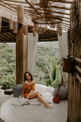 Young female in white shirt is having a relaxing morning drinking coffee in her hotel in Bali, Indonesia, surrounded by green lush landscape