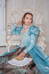 Beautiful young woman in medieval style blue dress on the floor near the armchair