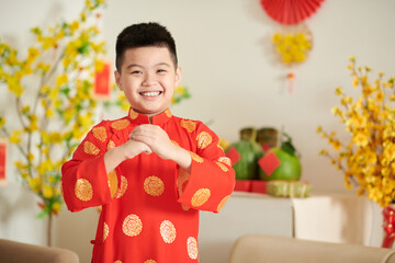Portrait of happy little Vietnamese boy in traditional Lunar New Year costume making greeting...