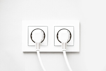 Electrical socket isolated on gray wall. White wire plug plugged in. Renovated studio apartment power supply background. Empty copy space double white plastic power outlet.