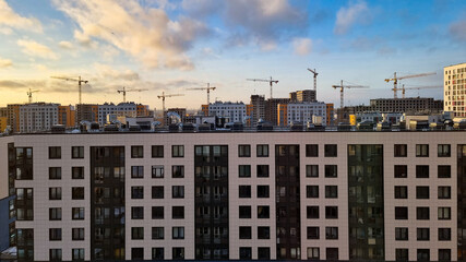 New construction site with tower cranes against the sky. Lots of tower cranes behind a new house. Construction of new residential buildings in the city.