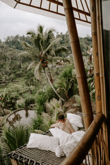 Young male traveller relaxing in a hotel in Bali, surrounded by nature, palm trees, rice fields and...