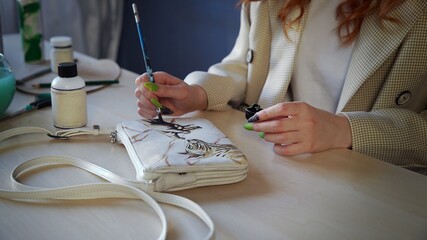 Obraz premium Close-up of a beautiful red-haired girl painting with multicolored paints on a bag. Handmade work