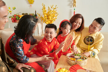 Happy family enjoying nuts and candied fruits with tea when celebrating Lunar New Year at home