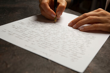 Naklejka premium The girl writes a letter. Cropped hands on the table with pen and paper.