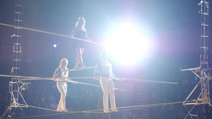 Performance of three aerial tightrope walkers gymnasts in white suits in the circus. Aerialists arrange a show for the audience under the dome of the circus, a tightrope walker walks on a rope.