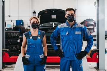 Male and female mechanics with protective face masks are working together in large modern car repair service.