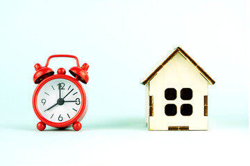 red alarm clock and wooden house, the concept of buying a new apartment in