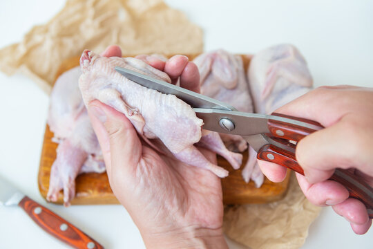 Raw quails lie on a wooden board. A man uses scissors to cut diet lean meat.
