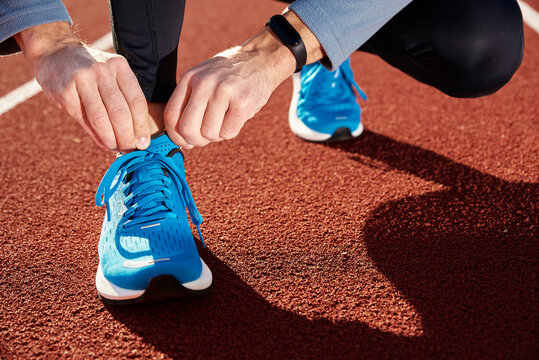 Male runner in blue sneakers get ready for run at stadium track, close up. Male hands tying on sport sneakers for jogging. Fitness and healthy lifestyle concept