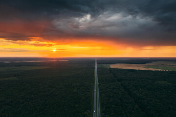 Aerial View Of Sunset Sky Above Highway Road Through Green Forest Landscape In Sunny Evening. Top View Of Highway Motorway Freeway From High Attitude In Summer Sunrise. Bird's Eye View