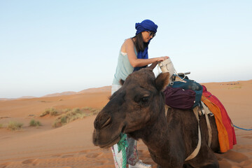 Caucasian middle aged woman packing to travel with a camel in the middle of the desert in October 