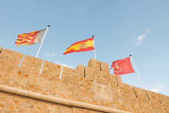 Spanish Flags Swaying On Gentle Breeze On Segorbe Castle In Spain. low angle