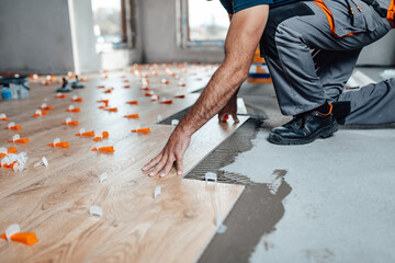 Flooring and tiling. Professional tiler placing floor tiles on adhesive surface. - obrazy, fototapety, plakaty