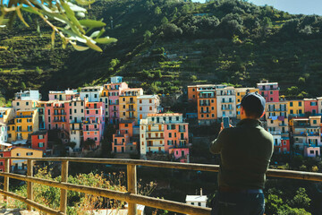 Selective focus on mobile phone, ataking photo at panoramic view of Riomaggiore colorful village, Cinque Terre, Italy