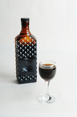 Coffee liqueur in dark glass bottle and filled shot glass. White background, isolated