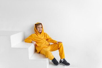 Fototapeta na wymiar a teenager in a yellow tracksuit on a monochrome background in a hood is sitting on the steps