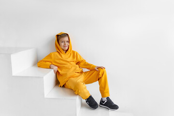 a teenager in a yellow tracksuit on a monochrome background in a hood is sitting on the steps