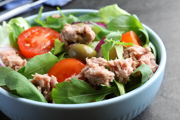 Bowl of delicious salad with canned tuna and vegetables on black table, closeup